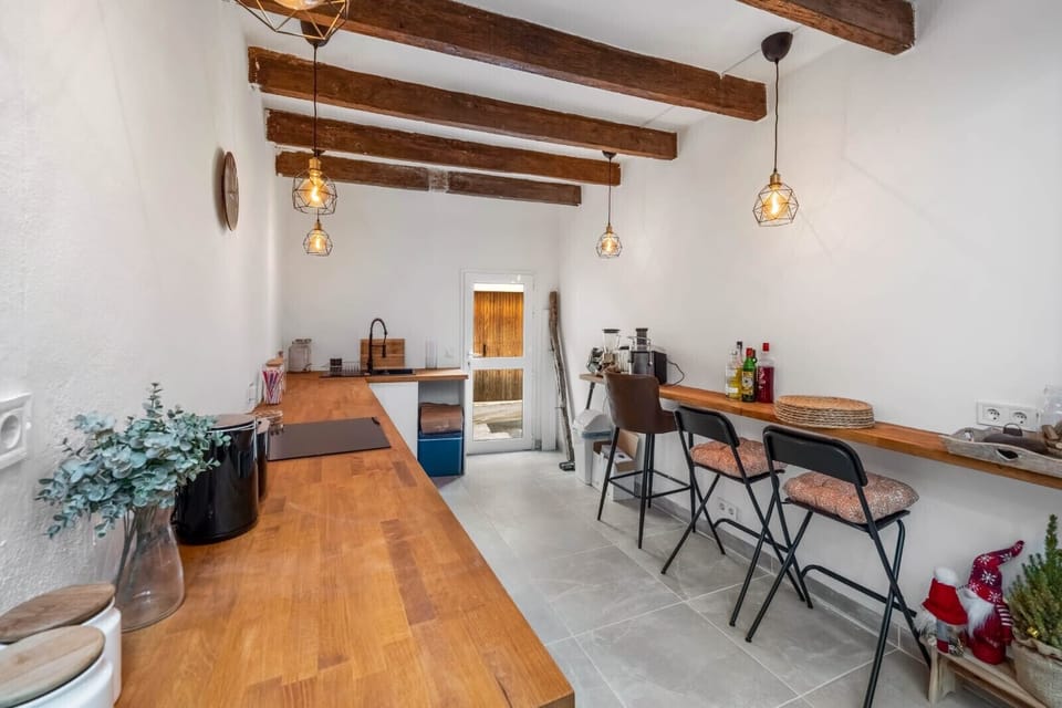 Elongated kitchen with wooden countertops, exposed beams and a bar area with stools, lit by pendant lights and offering direct access to the outdoor patio.