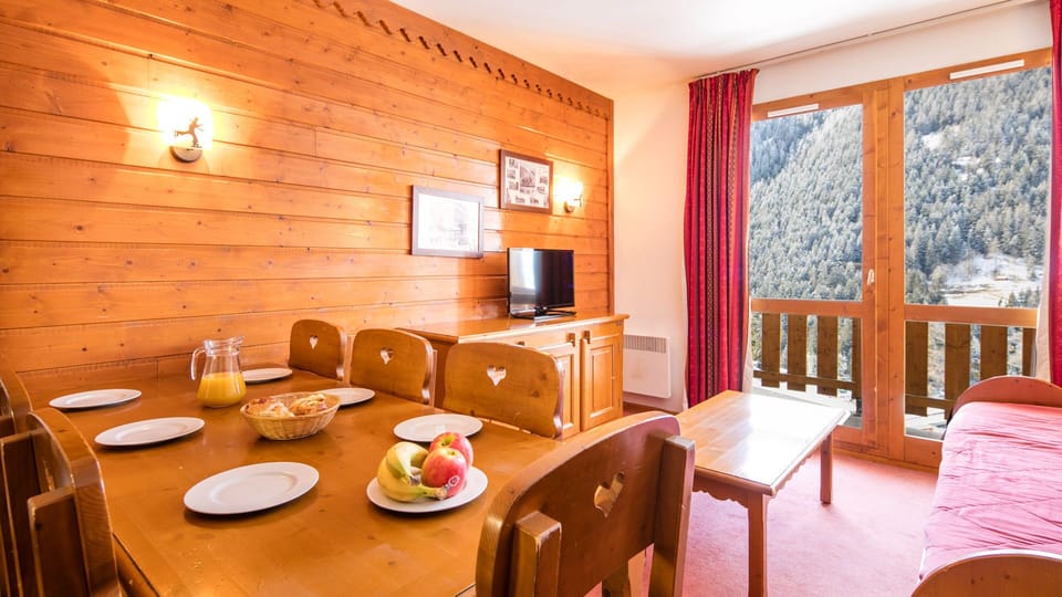 Bright alpine-style living room with dining table and balcony overlooking the mountains — perfect for cozy family meals.