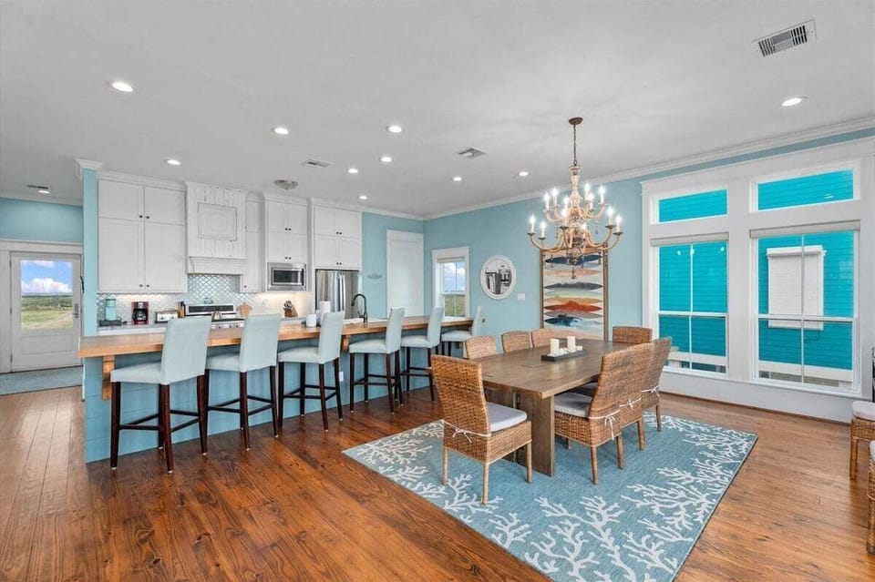 Open dining and kitchen area with large dining table, bar seating, and coastal luxury finishes