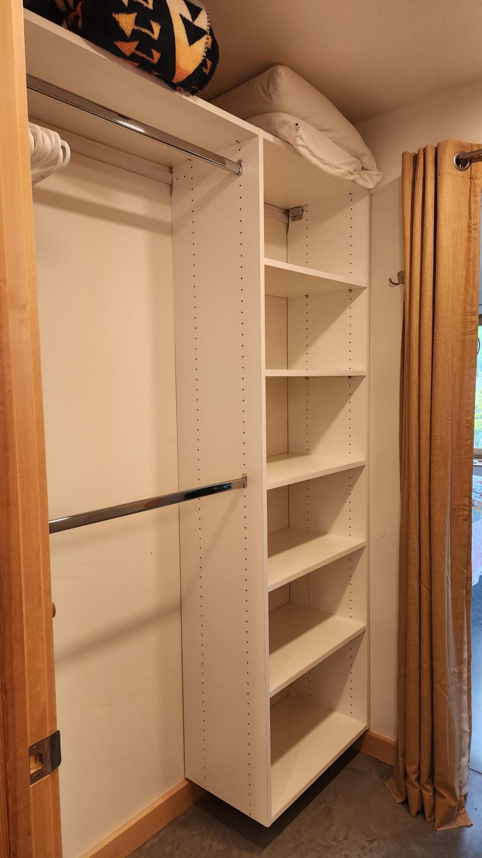 White built-in closet shelves and double hanging rods with a folded blanket and pillow on top.