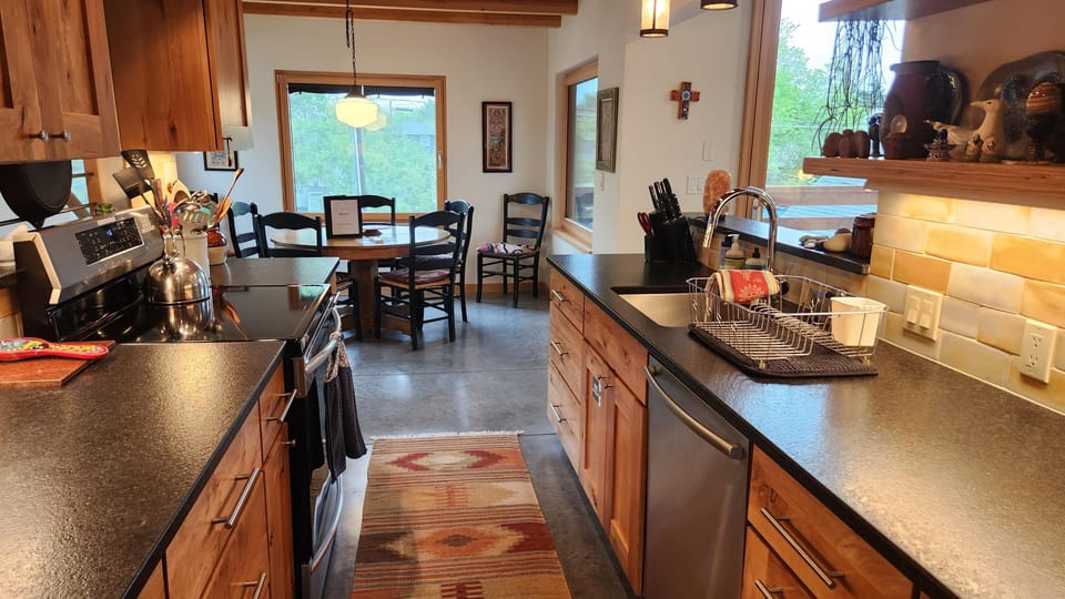 Galley kitchen with dark stone countertops, wooden cabinets, and a patterned runner leading to the dining area.