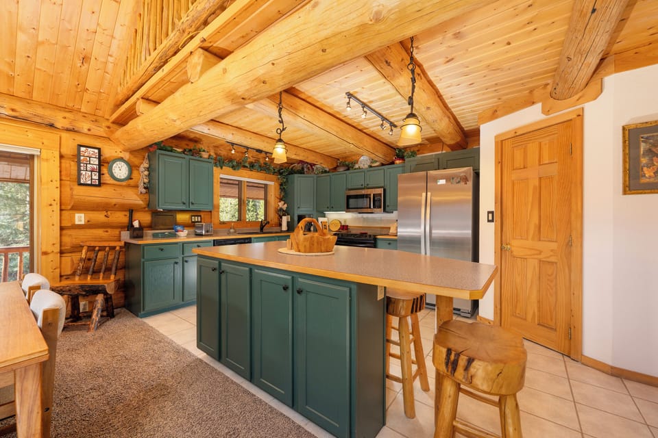 Step into your fully-equipped mountain kitchen with rustic beams, sage cabinetry, and stainless appliances—perfect for creating memorable meals together.