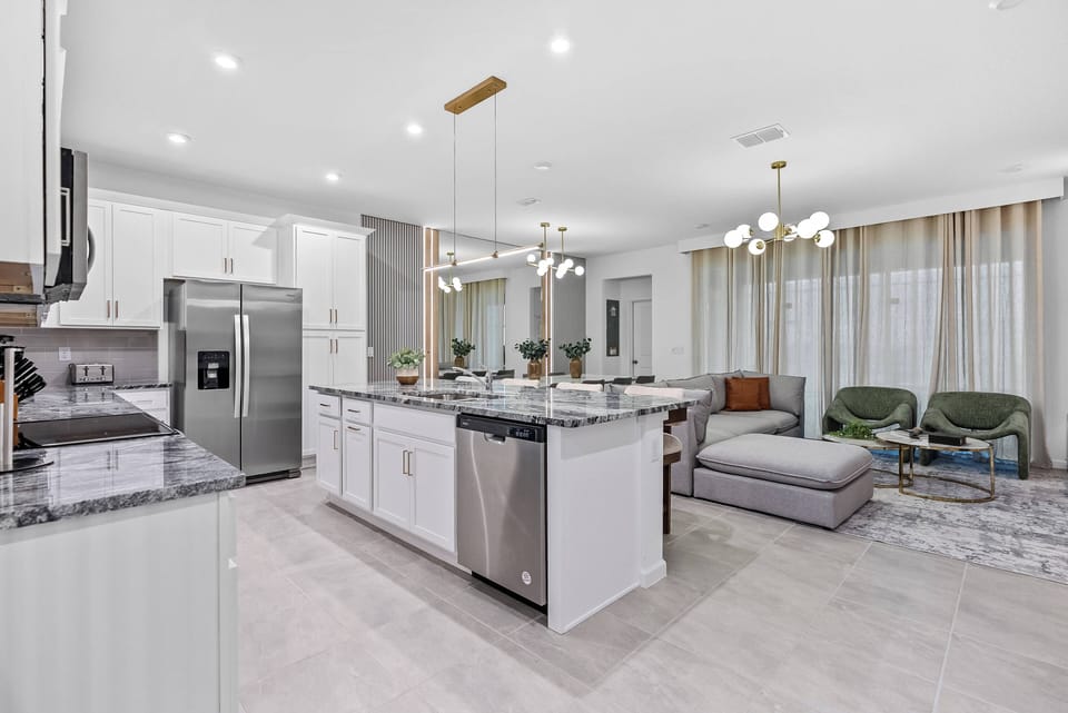 Step into this sophisticated kitchen and living area, where sleek white cabinetry meets stunning granite countertops. The warm glow of stylish pendant lights complements the modern furnishings, inviting you to relax and unwind.