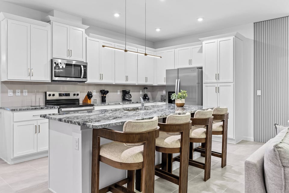 Enjoy a chic kitchen featuring sleek white cabinetry and elegant granite countertops. The spacious island with four modern bar stools is ideal for meal prep or casual dining, all illuminated by warm, cozy lighting.