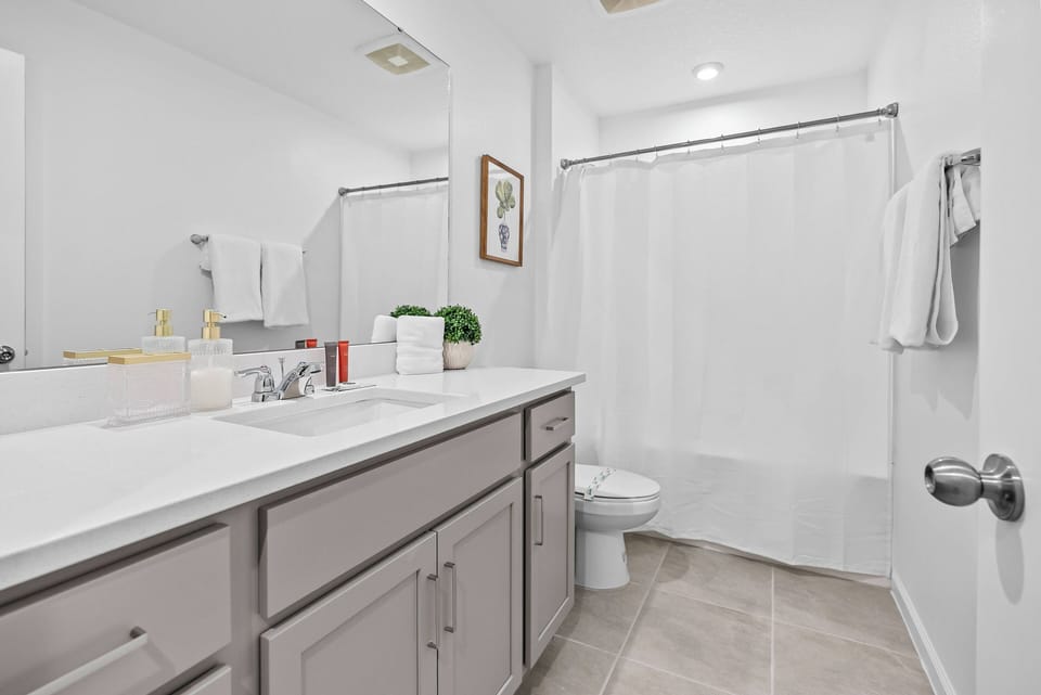Enjoy a refreshing bathroom with sleek gray cabinetry and a spacious white countertop that invites relaxation. Natural light brightens the modern space, enhanced by neatly arranged towels and tasteful decor for a polished feel.