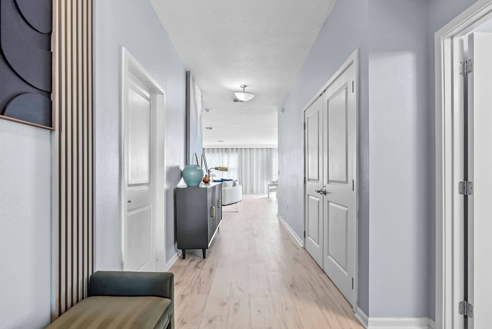Enter a welcoming hallway with calming blue walls and beautiful wood flooring leading to a bright living area filled with natural light.