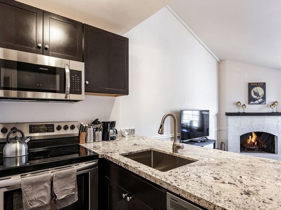 Fully stocked kitchen nook with a refrigerator/freezer, oven/range, microwave, dishwasher, coffee maker, keurig, toaster, blender, crockery (plates, bowls, cups), flatware (knives, forks, spoons) and cookware