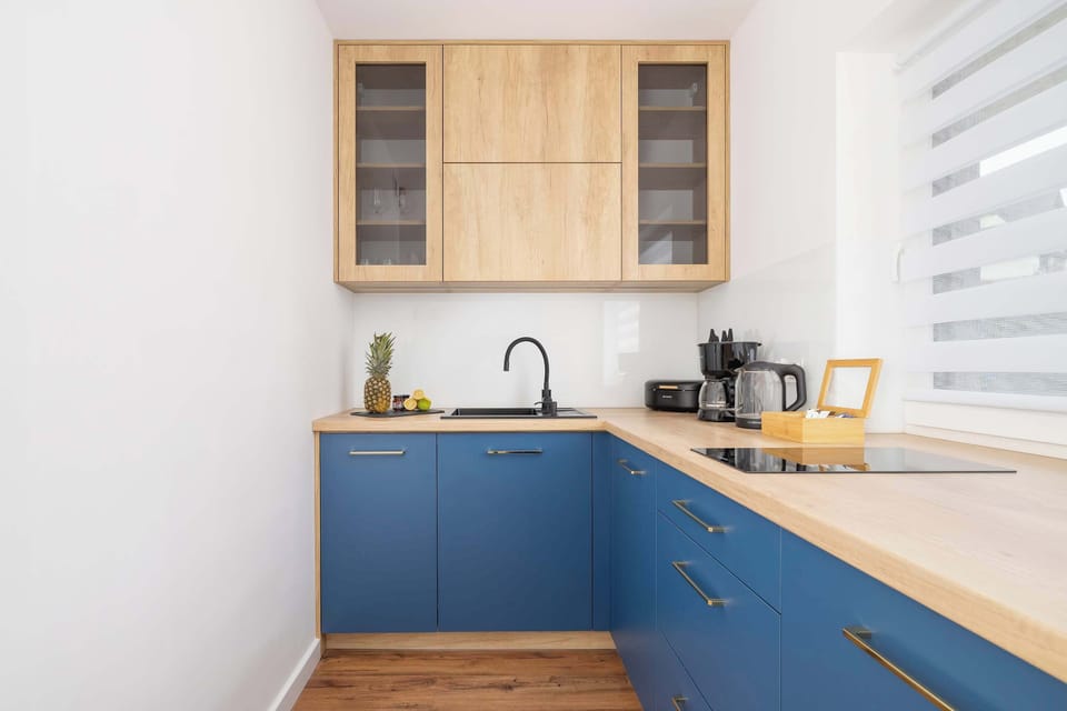 A compact kitchen with blue lower cabinets and light wooden upper cupboards. The clean lines and color contrast add character to the space.