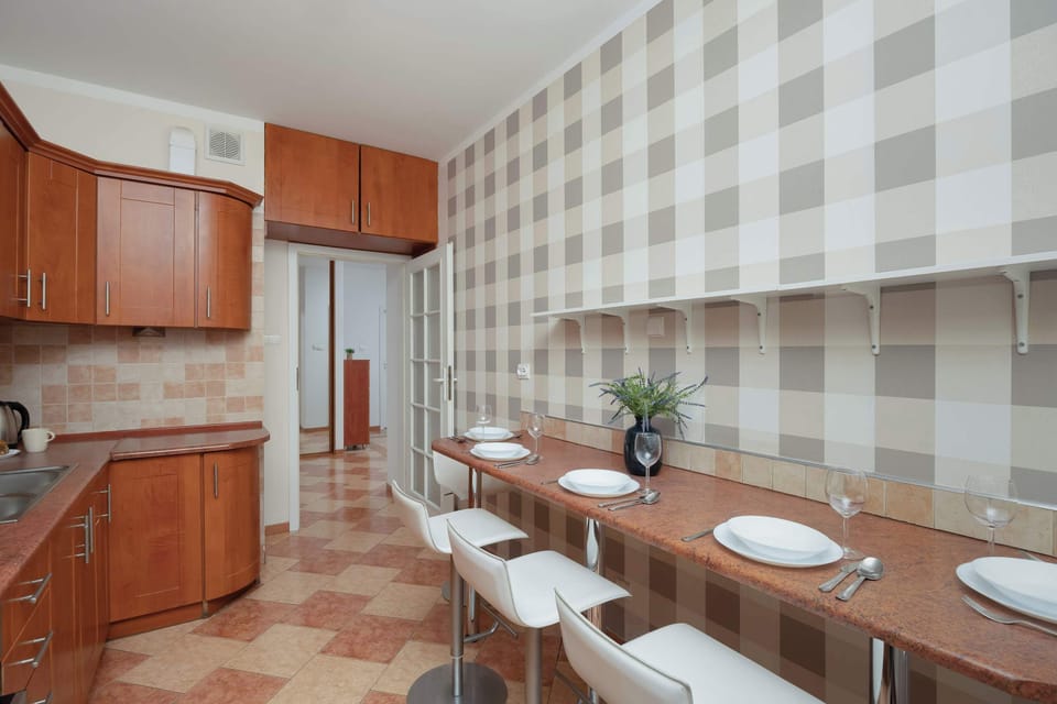 A  kitchen with wooden cabinets and a dining area featuring a table and four chairs. The design is warm and inviting with patterned wall tiles.