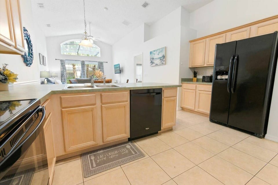 Step into a bright kitchen where soft beige cabinetry meets sleek black appliances, creating a balanced aesthetic. Large windows invite natural light, making it the ideal spot for morning coffee or preparing a family meal.