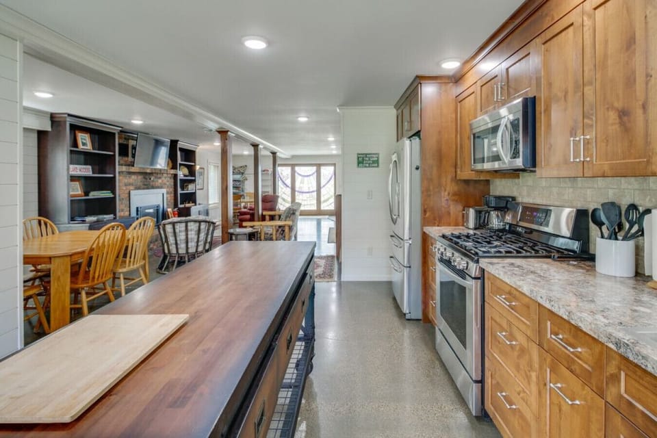 Open-concept kitchen & living | Stainless appliances, wood cabinetry, island, dining area, and cozy fireplace living room.