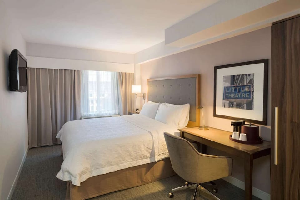 King bed guest room with desk, TV, and large window with curtains