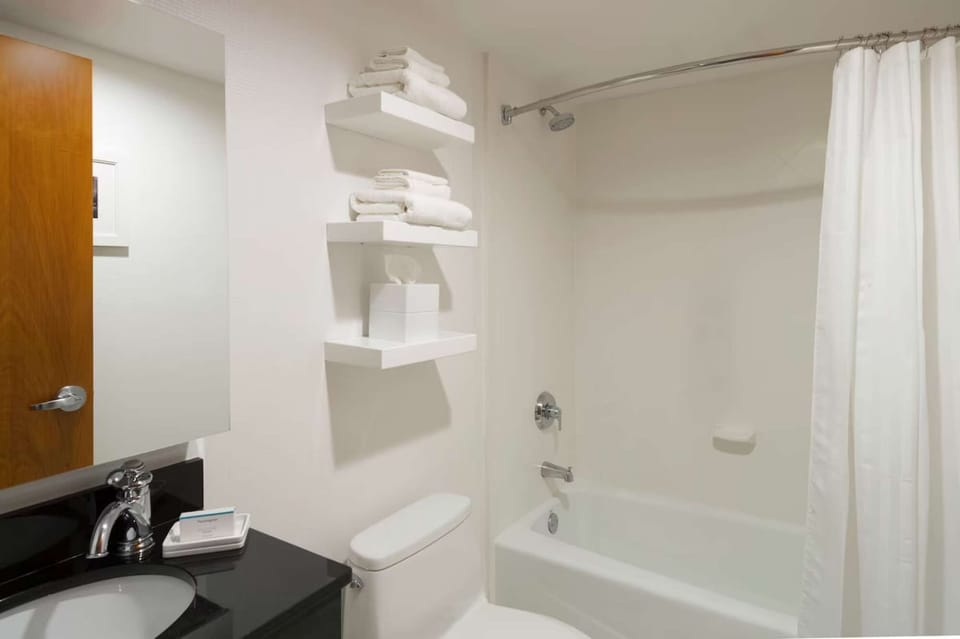 Clean bathroom with tub, shower, and fresh towels on shelves