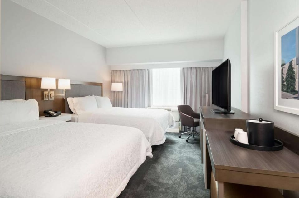 Room with two queen beds, desk, TV, and bright natural lighting
