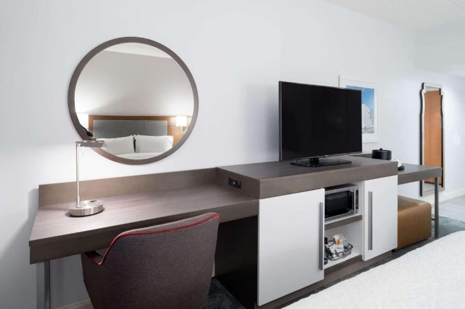 Work desk with round mirror, TV, and lamp beside the bed