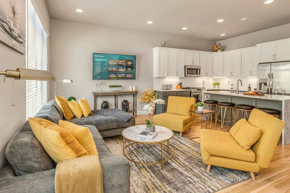 A grey sectional and mustard armchairs face the TV in an easy-flowing living room that keeps groups of friends and family connected during downtime