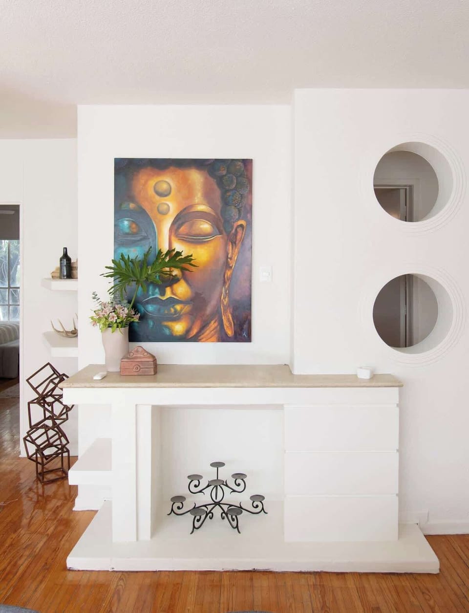 Artistic corner with a decorative white fireplace, bold wall art, and circular mirrors. Greenery and unique details add warmth to this stylish gallery-inspired home.