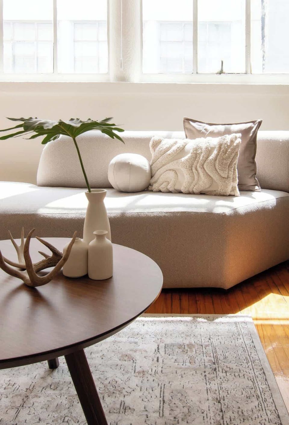 Soft natural light highlights the curved sofa with textured cushions and elegant decor on the coffee table, creating a serene and inviting corner to unwind.