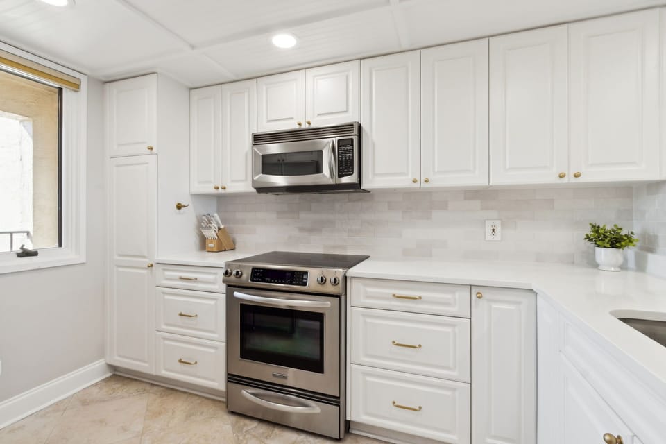 Luxury Remodeled Kitchen with Stainless Steel Appliances, Stunning White Cabinetry, Quartz Countertops, Gold Finishes and a Trendy Backsplash