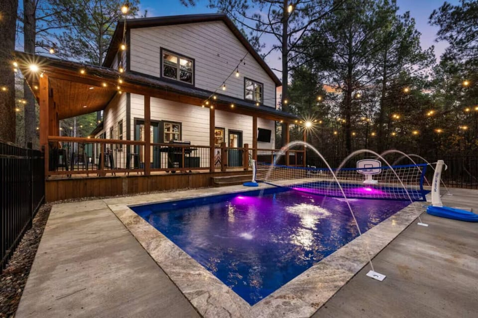 Heated pool glow at Poolside Par‑Tee—fountain jets, color‑changing lights, and the cabin shining behind you. You arrive to a private resort vibe made for late swims, laughter, and a deep exhale.