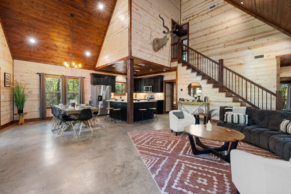 Open-concept great room with soaring ceilings, modern cabin finishes, and seamless flow from kitchen to dining and living areas, ideal for gathering after a day on the lake or hiking trails