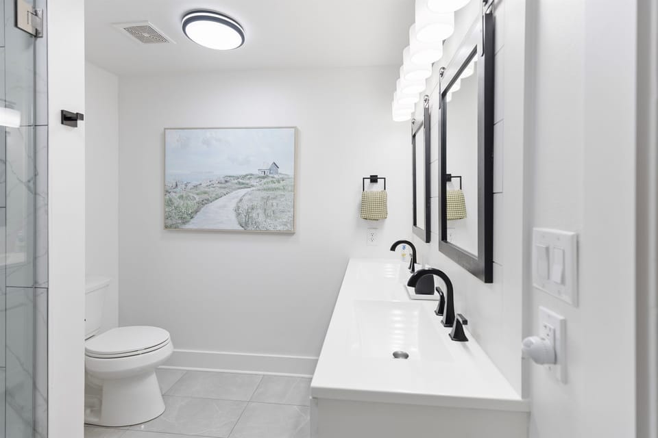 Unwind in your elegant bathroom sanctuary with modern fixtures, coastal artwork, and a refreshing glass shower for your perfect getaway.