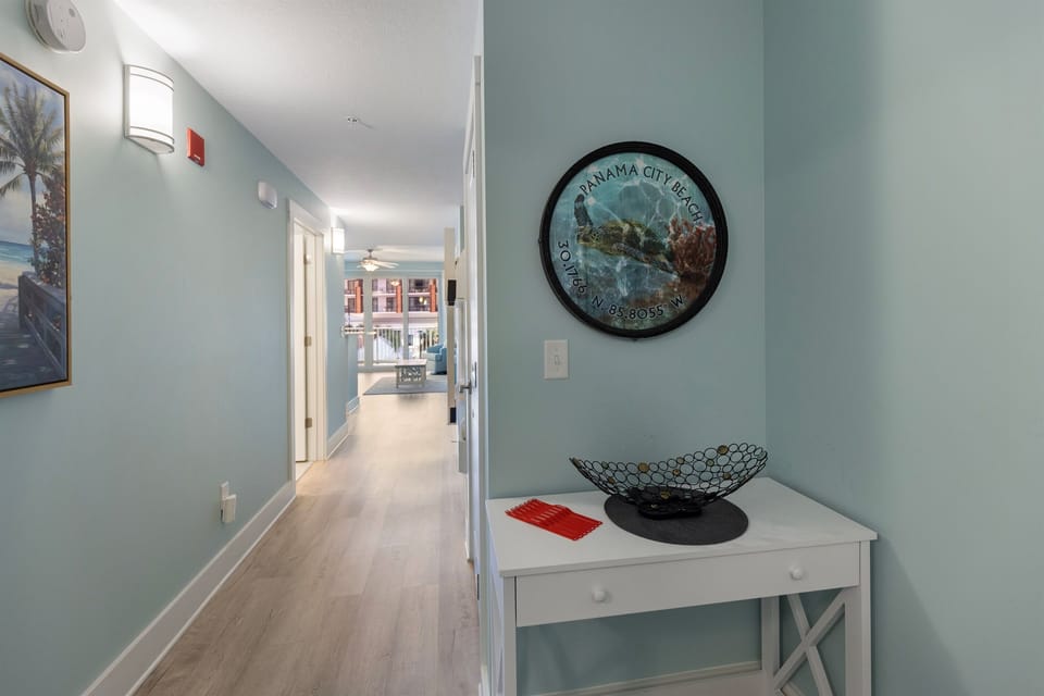 Walk through your bright, coastal-themed hallway where soothing blue walls and warm wood floors guide you toward relaxing spaces ahead.