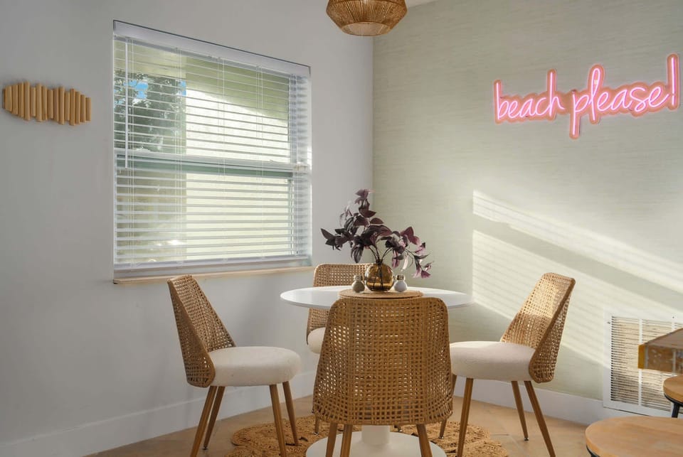 Charming dining nook with coastal flair, rattan seating, and playful “beach please” neon sign. Sunlit and stylish, it’s the perfect spot for morning coffee, casual meals, or planning your next sunny adventure.