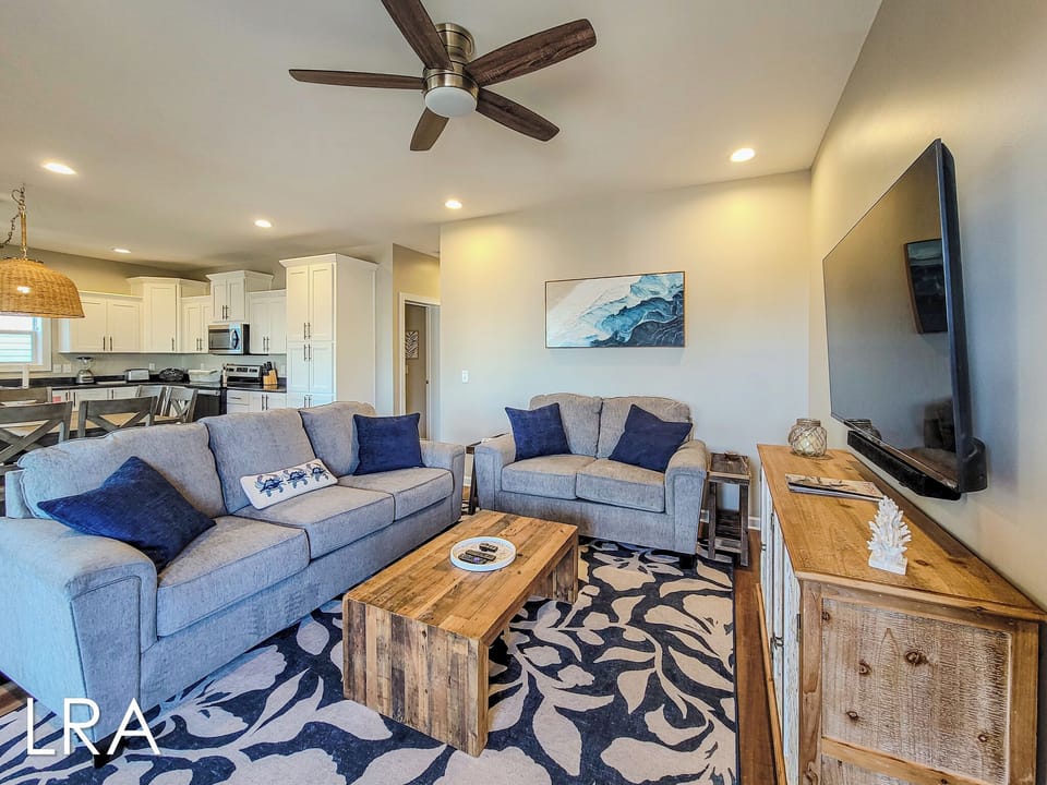 Sink into plush sofas in your open-concept living space, where coastal blues meet warm wood tones under a gentle ceiling fan breeze.