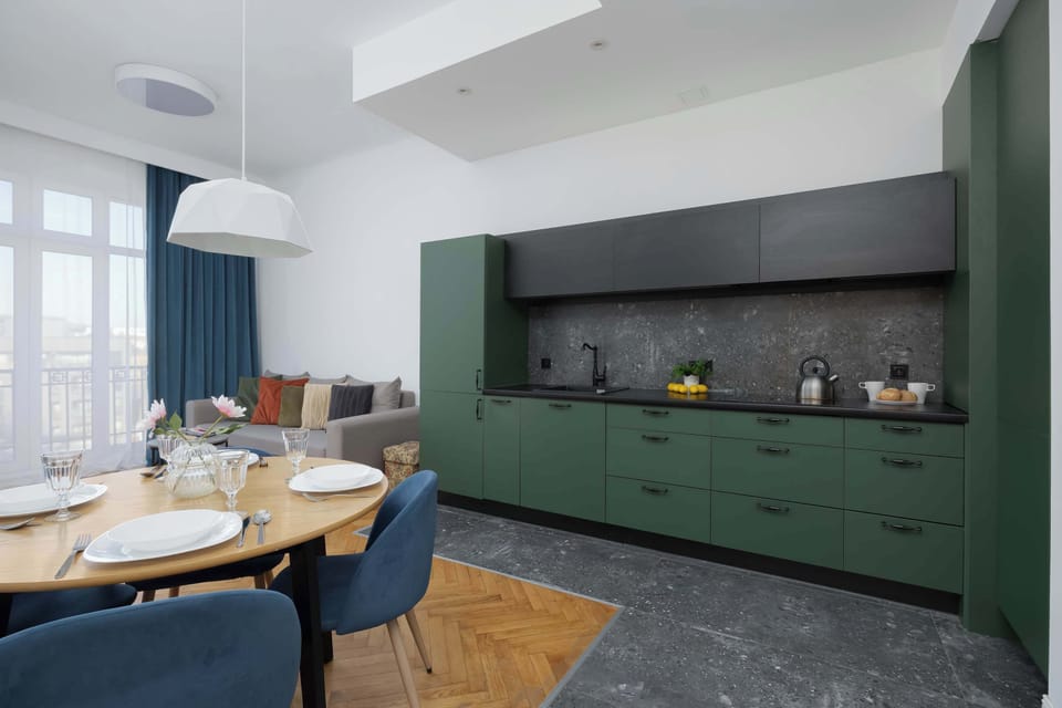 A dining corner with a round table, blue chairs, and a green kitchen in the background. The setting feels both cozy and functional.
