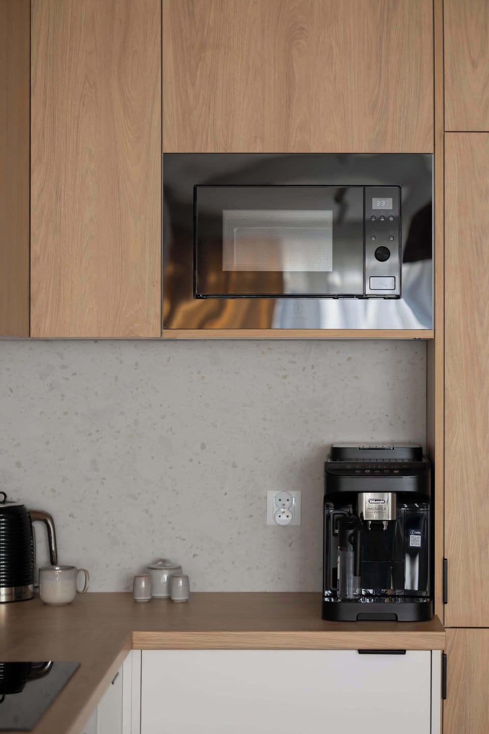 A small kitchen area with a coffee machine and wooden shelves. The layout is compact and efficient.