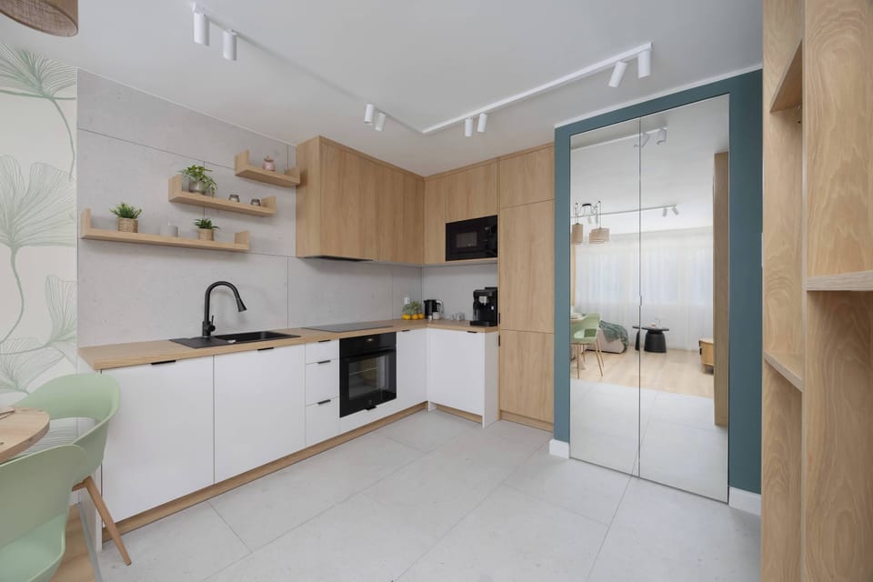 A stylish white and wood kitchen with clean lines and black fixtures. The bright lighting makes it look airy and functional.