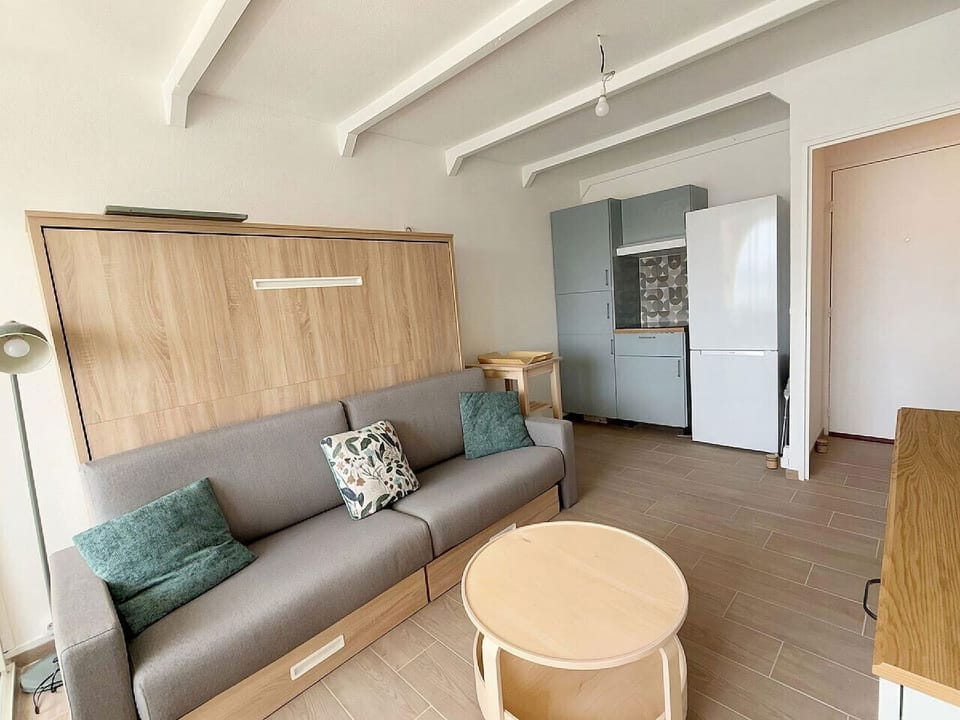 Espace de vie polyvalent – lit escamotable bois clair, canapé confortable et kitchenette intégrée. Chaque centimètre optimisé pour votre confort dans cet appartement vue port à Leucate.