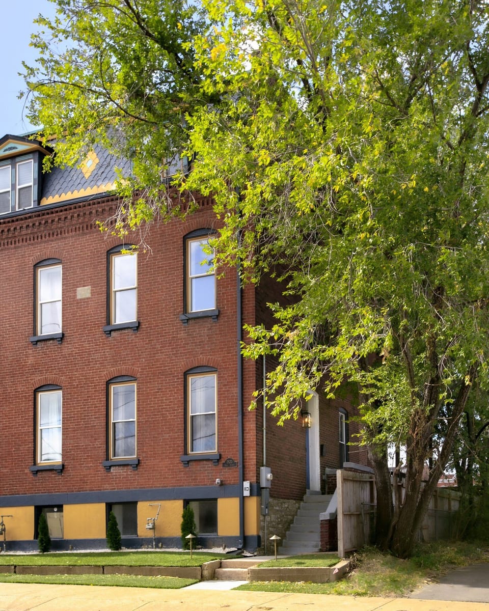 The multi-story brick residence presents a classic city facade shaded by mature trees.