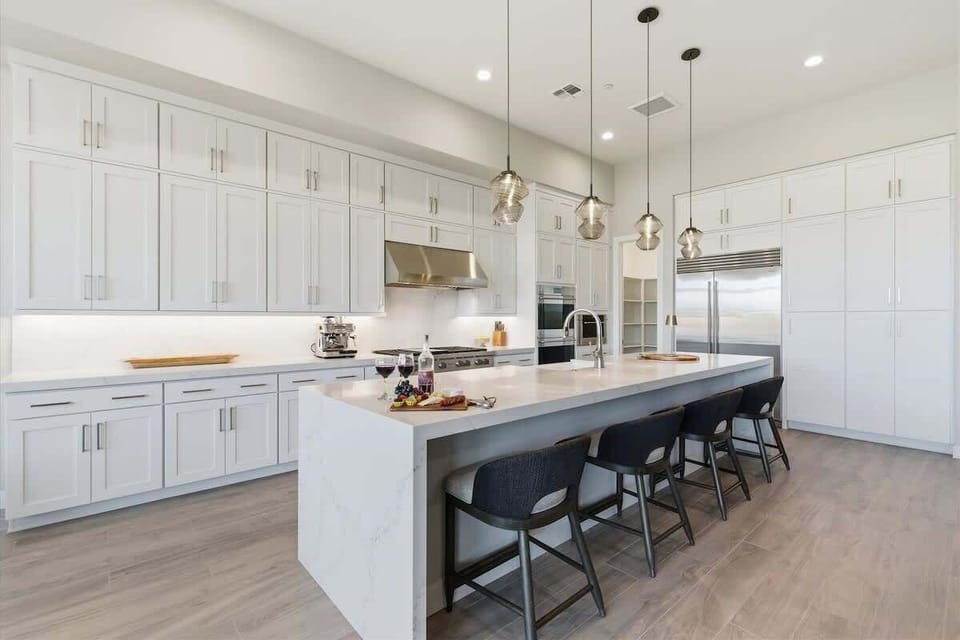 Full Kitchen features sleek white cabinetry, a spacious waterfall island with seating, and modern stainless steel appliances perfect for cooking and gathering.