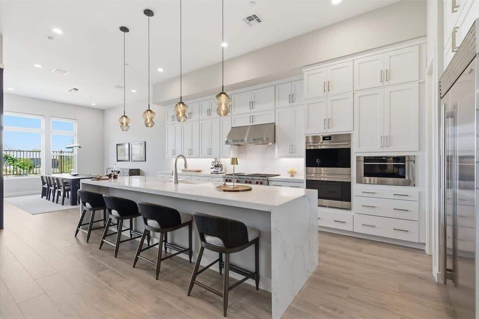 Full Kitchen features sleek white cabinetry, a spacious waterfall island with seating, and modern stainless steel appliances perfect for cooking and gathering.