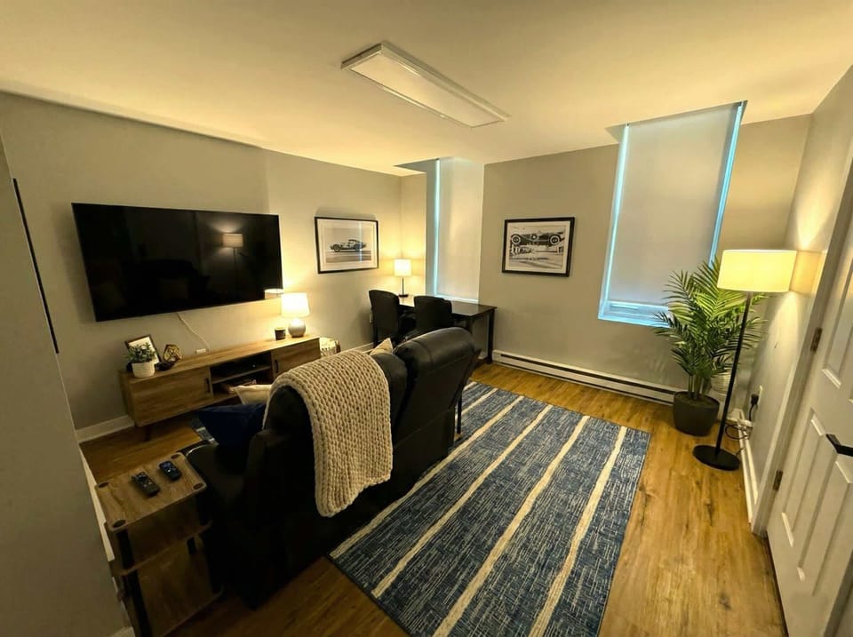 Living room view with wall-mounted TV, leather seating, windows, and floor lamp.