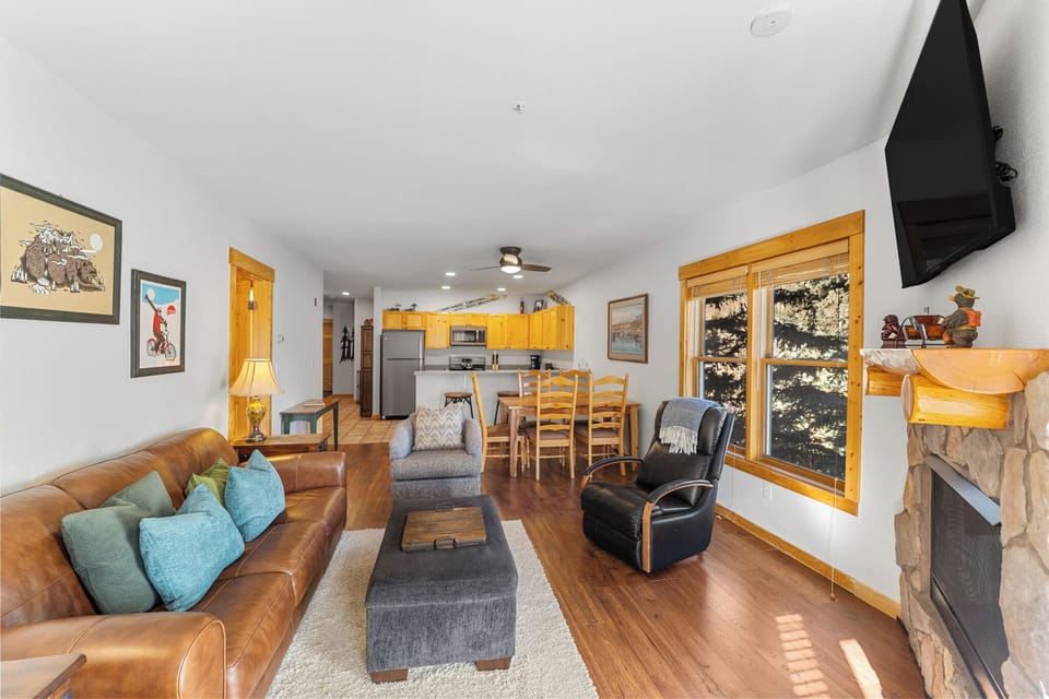 Relax in your open-concept living space featuring rich leather seating, a cozy fireplace, and stunning mountain views through oversized windows.