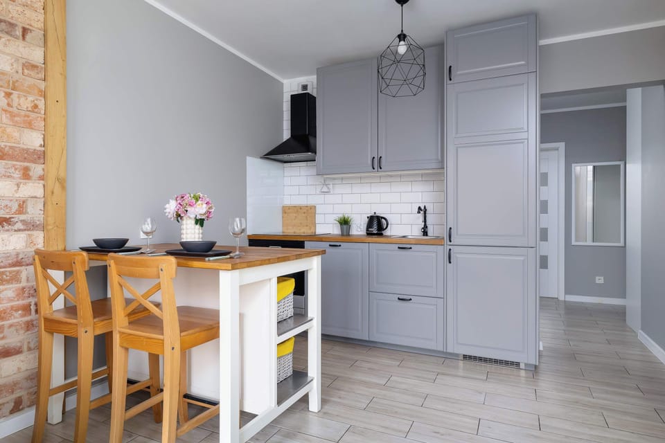 A kitchenette with gray cabinets, a wooden dining table, and chairs. The brick accent wall adds a stylish touch.