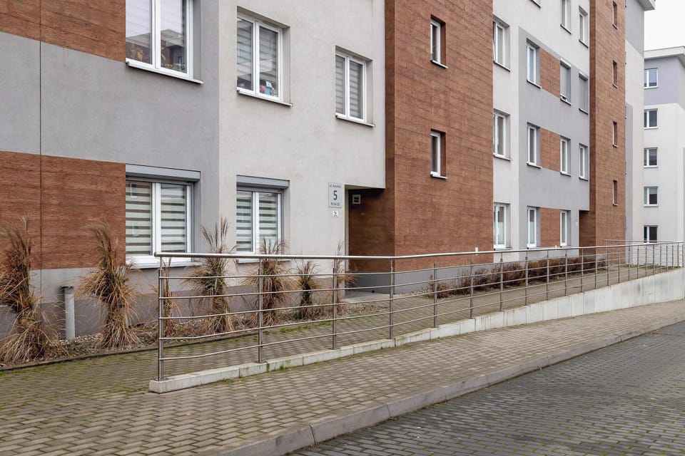 Another exterior view of the building showing the sidewalk and surrounding area. Low-rise residential buildings dominate the street.