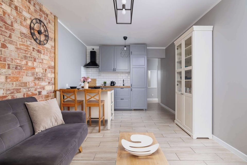 A living and dining space with a sofa, coffee table, and wooden dining table. Bright and modern design with brick accents.