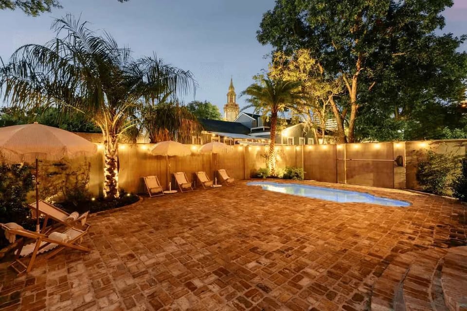 Evening view of the private backyard with brick patio, pool, hot tub, and ambient lighting.