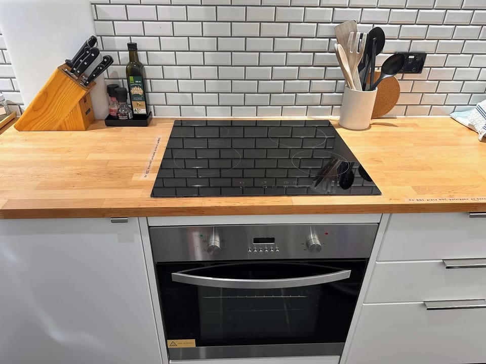 Kitchen close-up with cooktop, oven, knife block, and wooden benchtop.