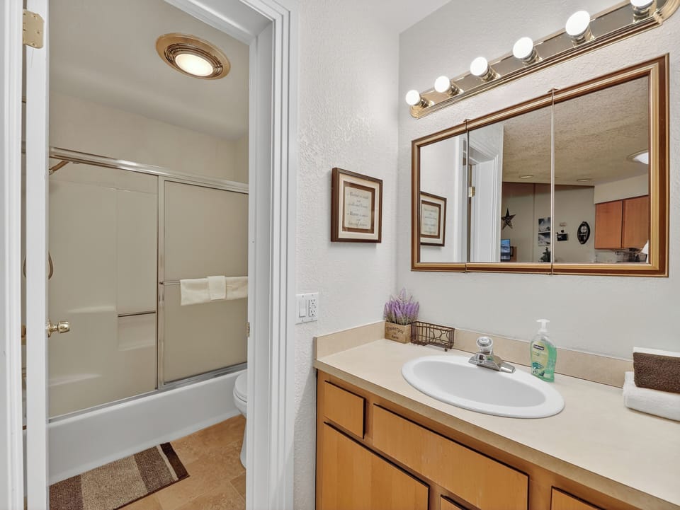 Your private bathroom features warm wood vanity and lighting for getting ready, with a spacious tub-shower combo.