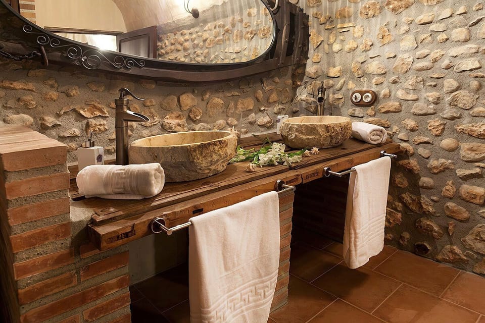 Refresh in a bathroom that blends rustic charm with modern comfort, featuring unique stone vessel sinks and an exposed stone wall.