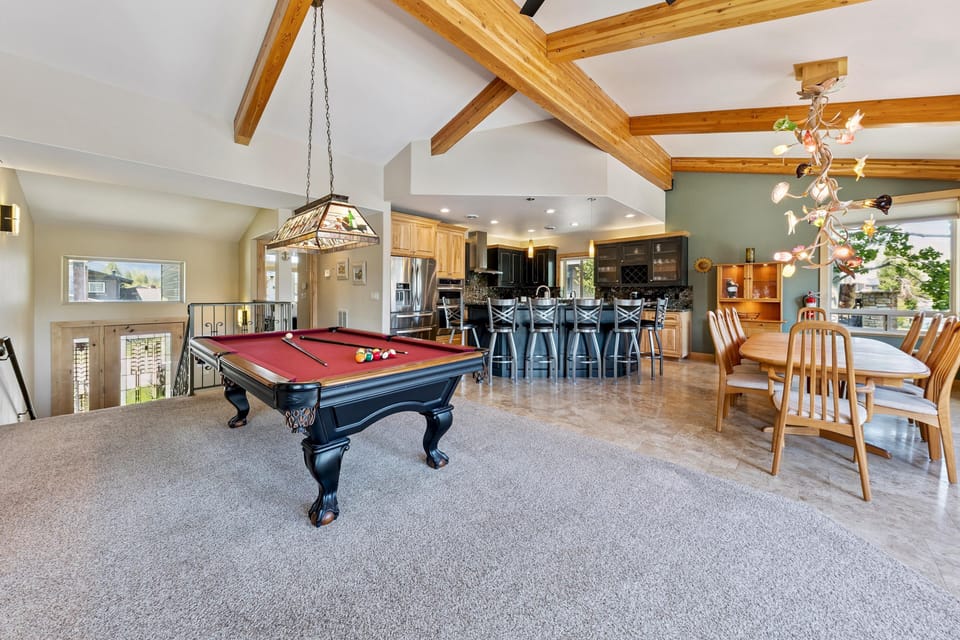 Billiards table with burgundy felt sits on carpeted floor beneath exposed wood beams and stained glass light fixture.