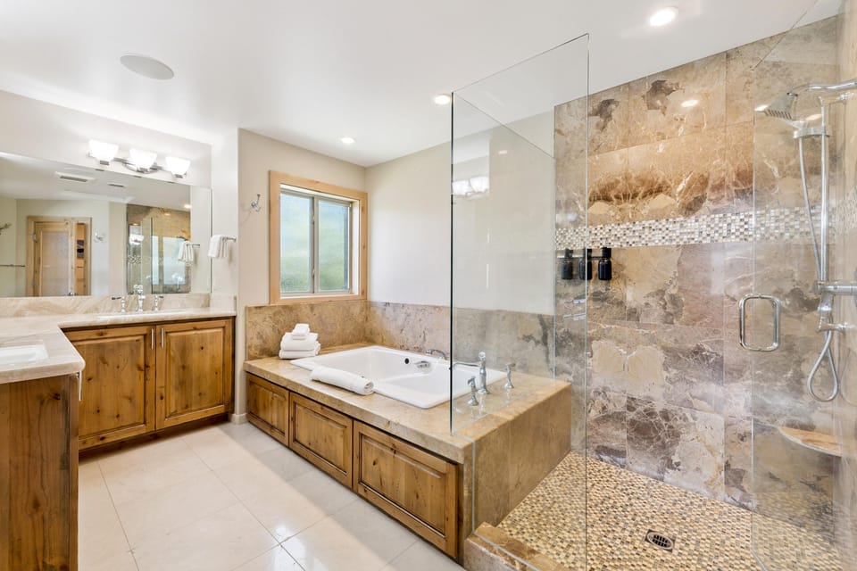 Bathroom features a large soaking tub with wooden paneling, marble surround, and a glass-enclosed stone-tiled shower.