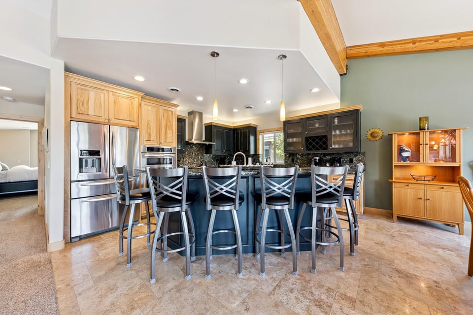 Kitchen island with six metal bar stools and black granite countertops beneath pendant lights and wood ceiling beams.