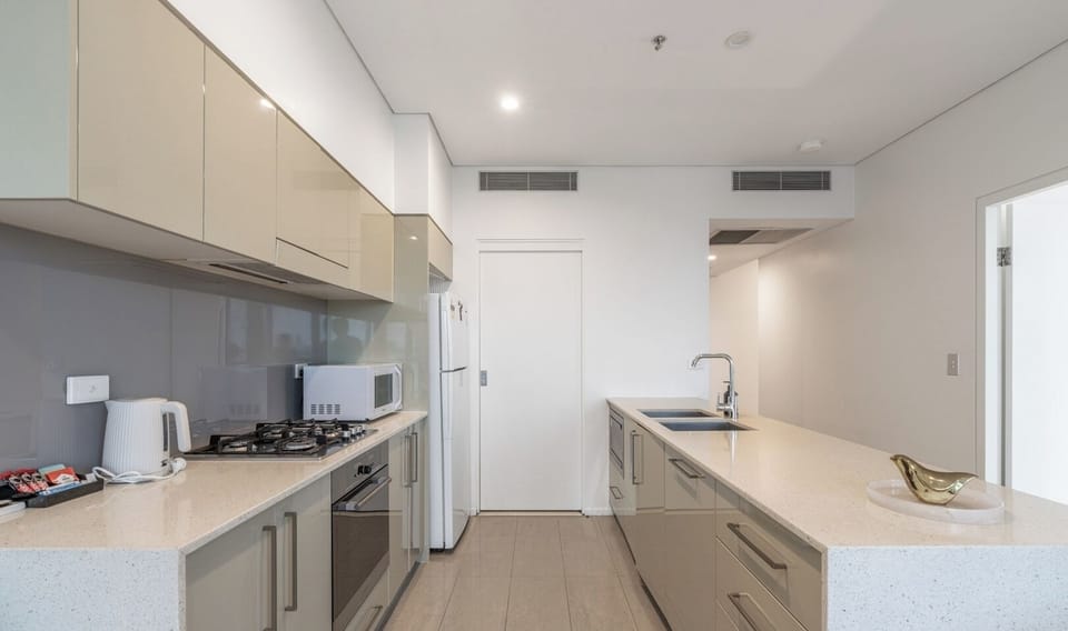 narrow, ultra-modern kitchen corridor equipped with glossy beige cabinetry, premium stone countertops