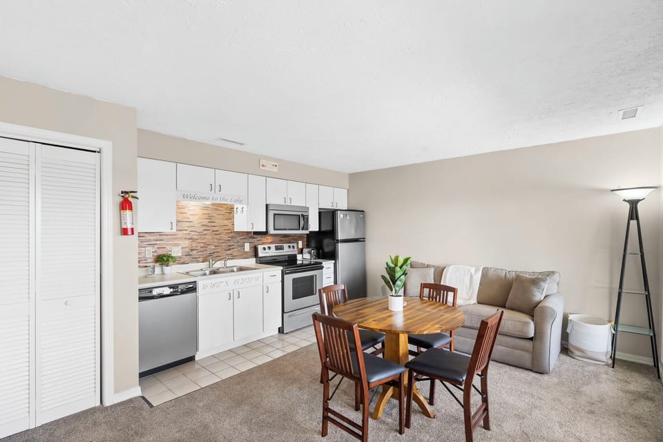 The open floor plan features a fully equipped kitchen, a dining table, a living area with a sleeper sofa and patio access, a bedroom, and a bathroom.